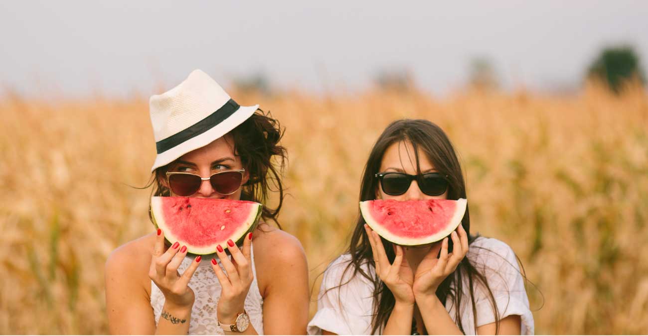 Zwei Frauen halten sich eine Scheibe Wassermelone vor das Gesicht